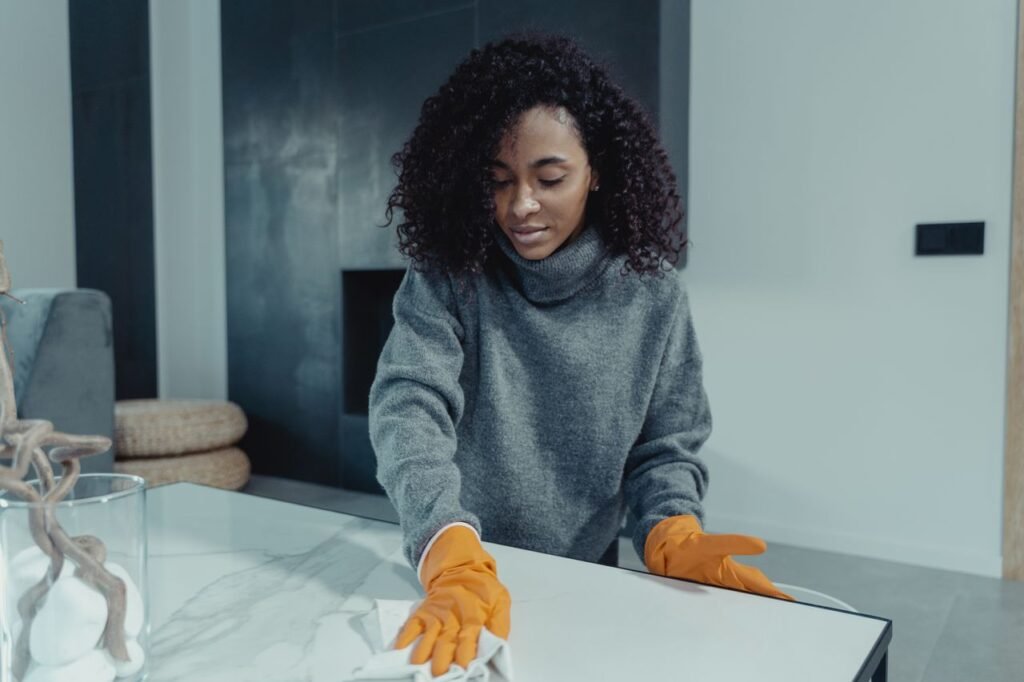 Woman wearing gloves wipes a table in a cozy modern living room.